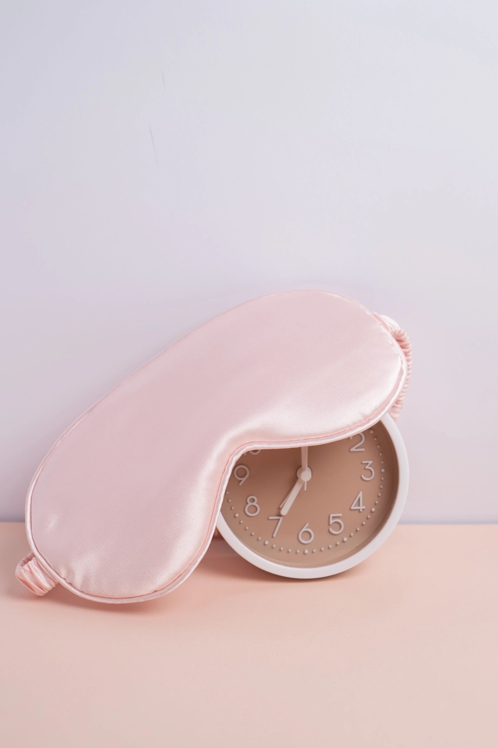 Pink silk sleep mask resting over an alarm clock