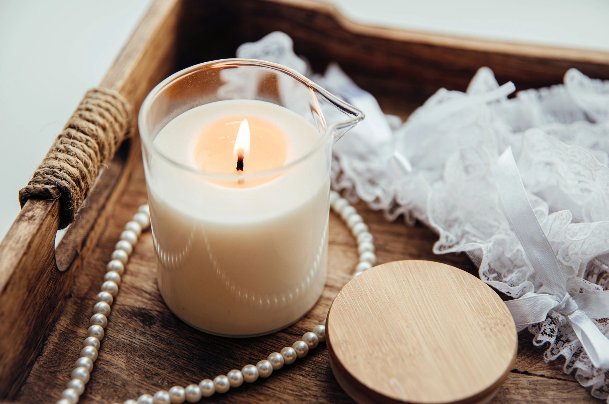 Massage candle, pearl necklace, and white lace lingerie arranged on a tray