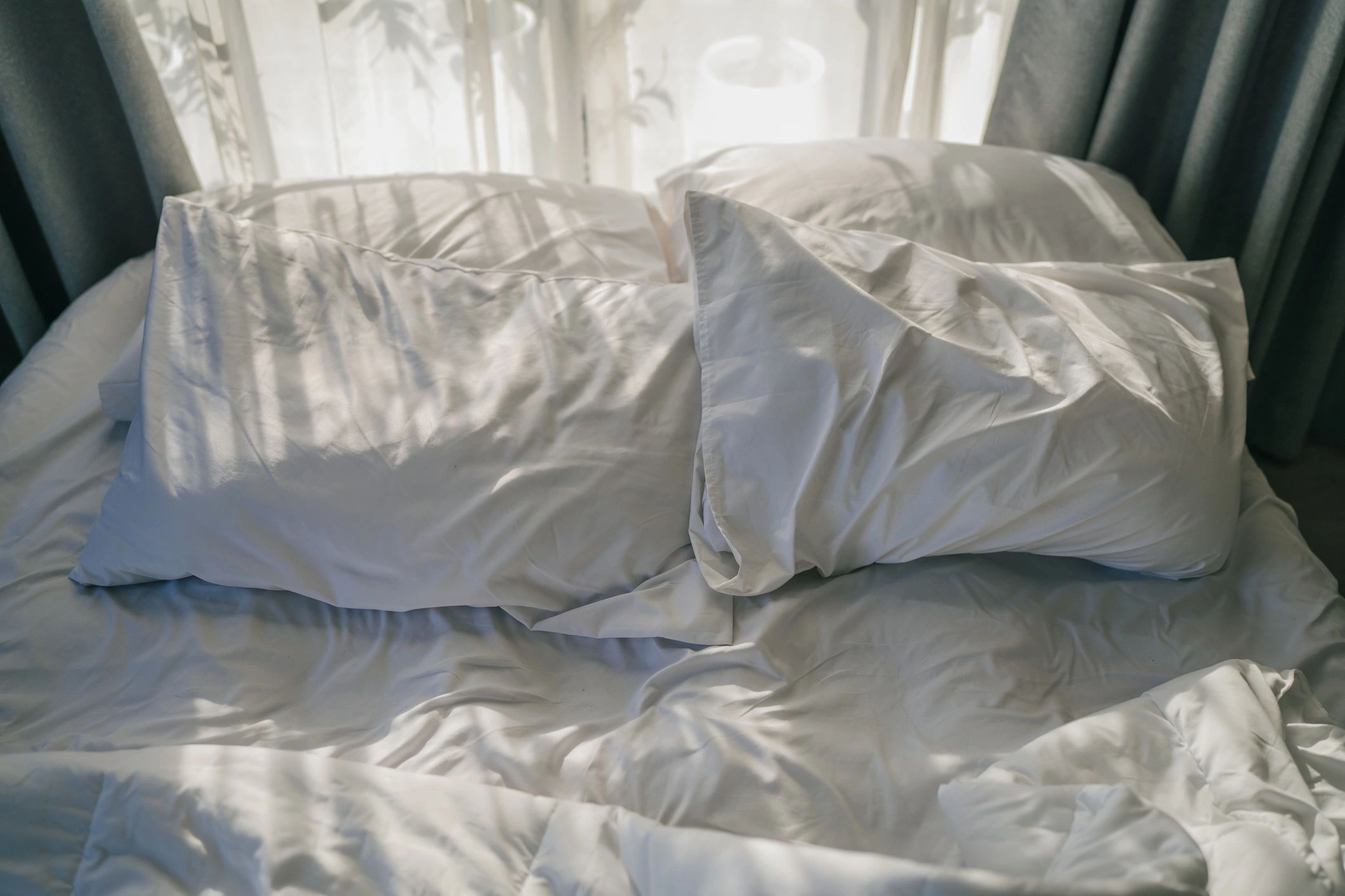 Rumpled white bed linens in morning sunlight
